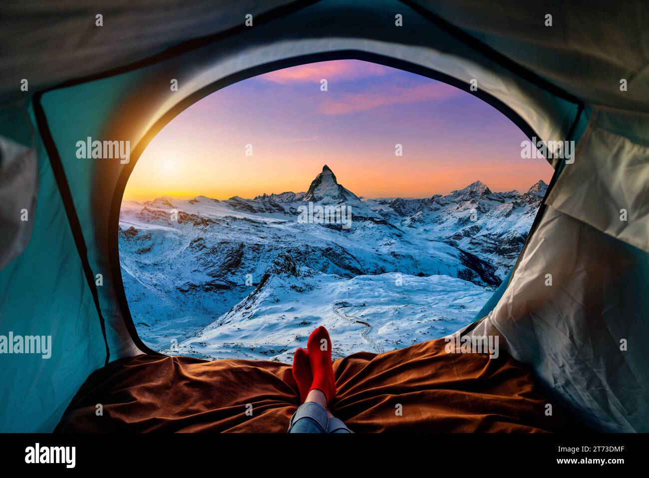 Frau mit Kreuzbein auf Decke im Campingzelt mit Schlafsäcken auf dem Berghang. Blick von innen auf das Matterhorn. Stockfoto