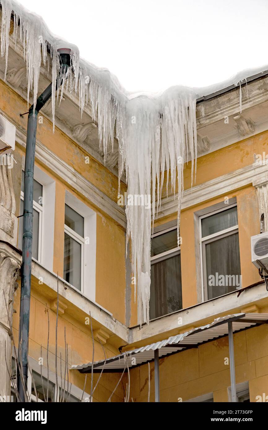 Riesige Eiszapfen hängen an den Traufen von Gebäuden und drohen während des Auftauens einzustürzen Stockfoto