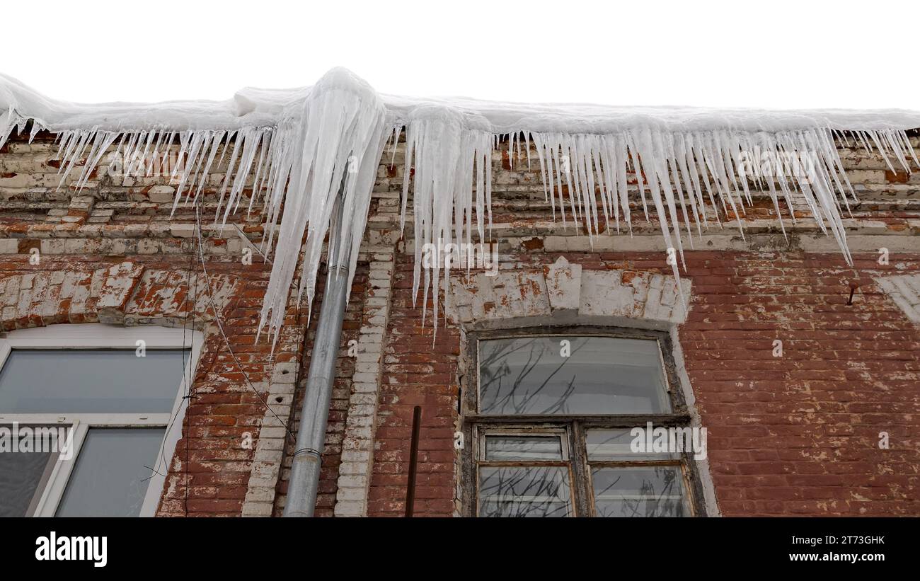 Riesige Eiszapfen hängen an der Traufe eines alten Gebäudes und drohen zu fallen. Stockfoto