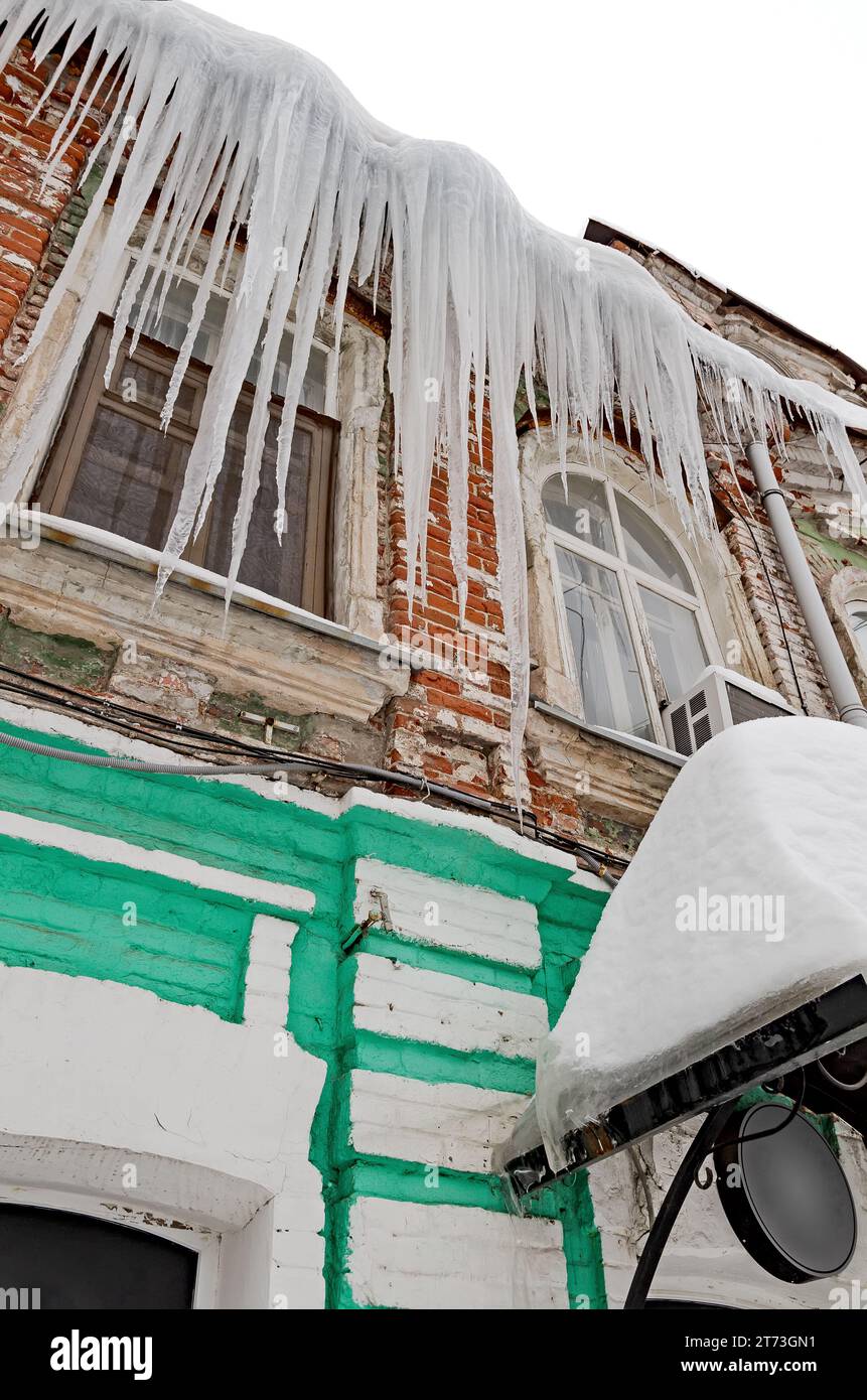 Riesige scharfe Eiszapfen hängen gefährlich vom Dach eines alten Hauses. Stockfoto