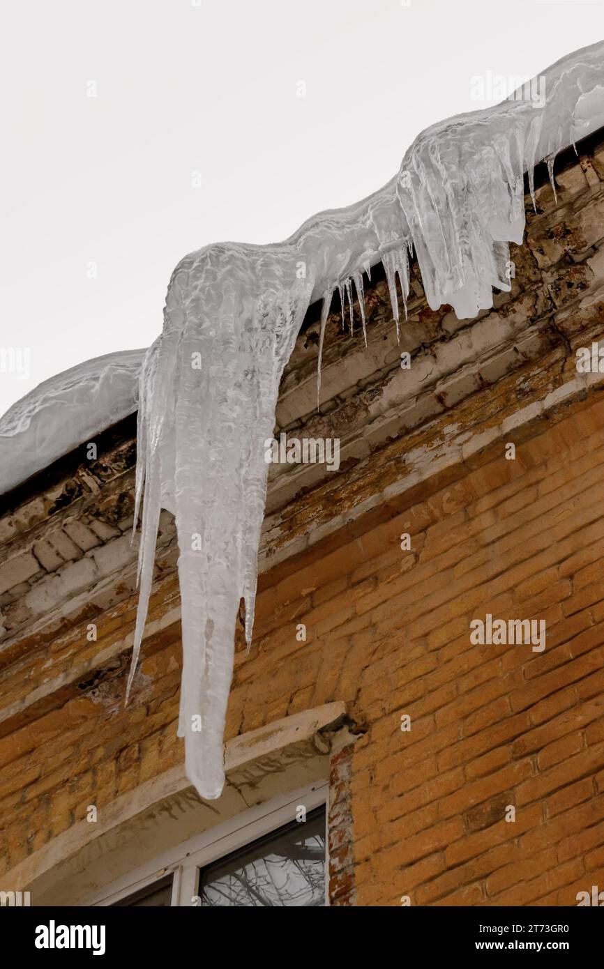 Ein riesiger Eiszapfen (Eisblock) hängt vom Dach eines Backsteinhauses. Stockfoto