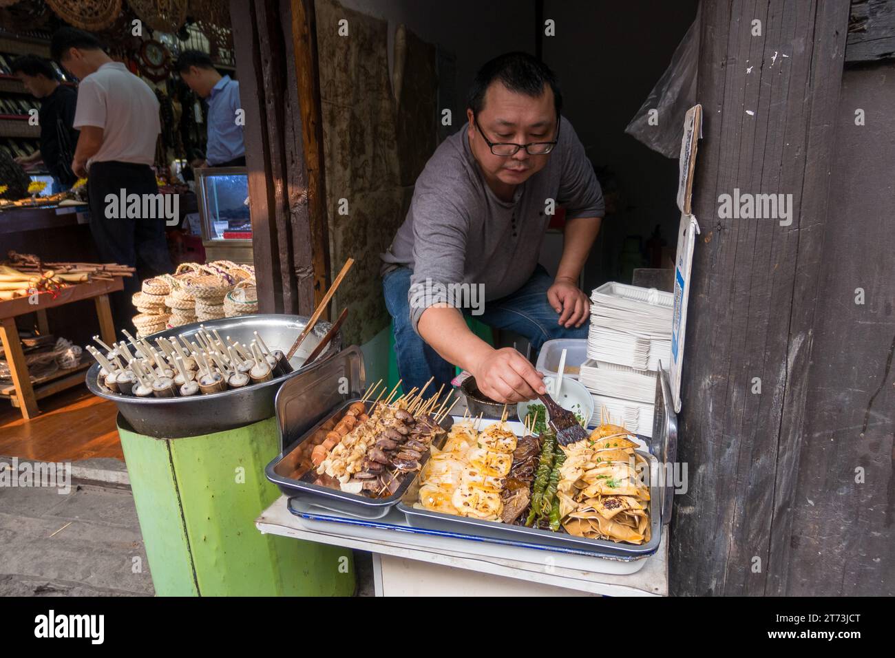 Restaurateur, der auf einem chinesischen Markt Soße auf Essen zum Mitnehmen streut. Stockfoto
