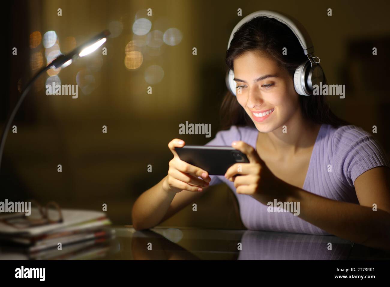 Glückliche Frau, die nachts Kopfhörer trägt und sich Videos auf dem Telefon zuhause ansieht Stockfoto