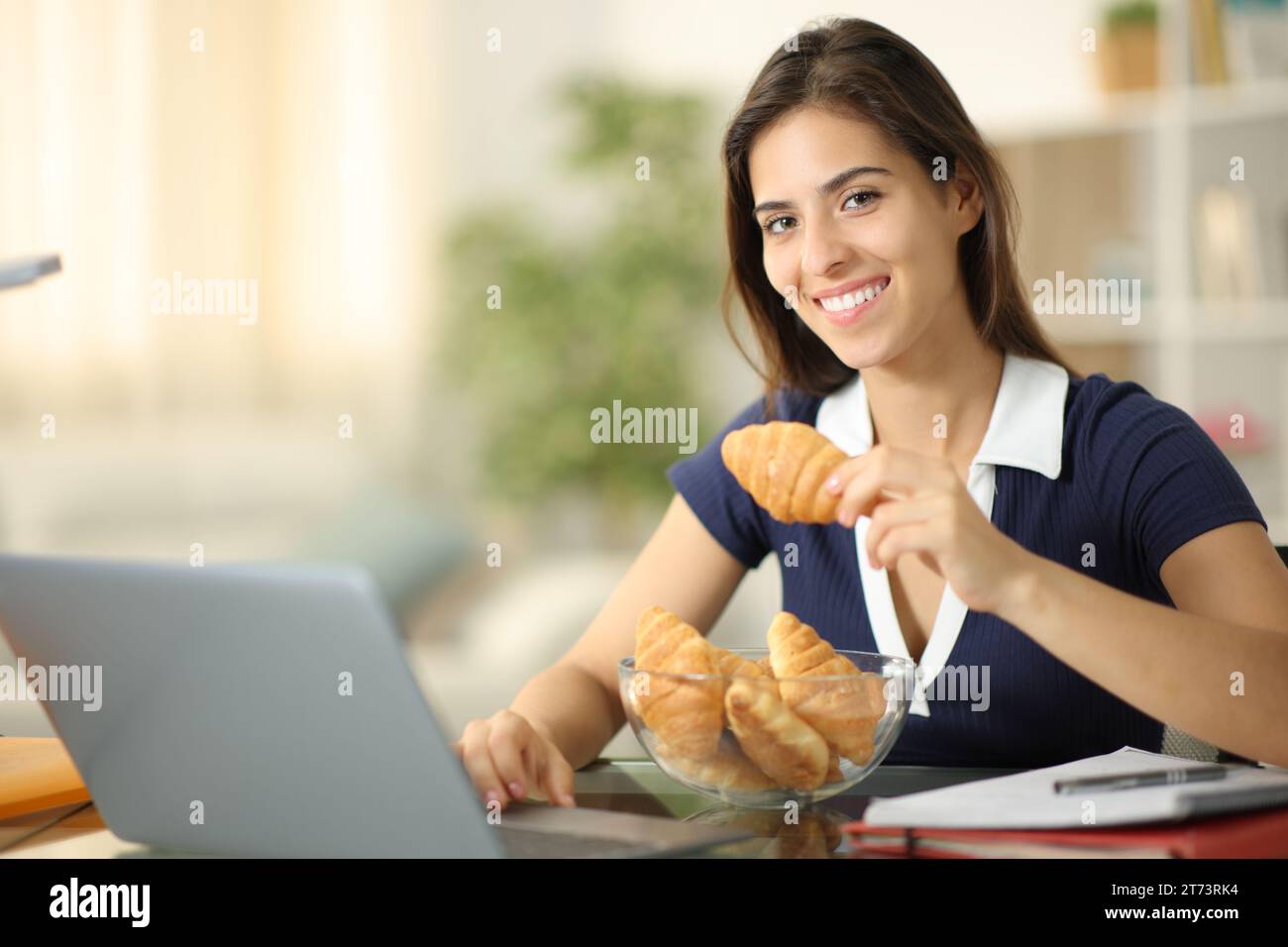 Fröhliche Schüler-E-Learning beim Essen von Croissants, die zu Hause in die Kamera schauen Stockfoto