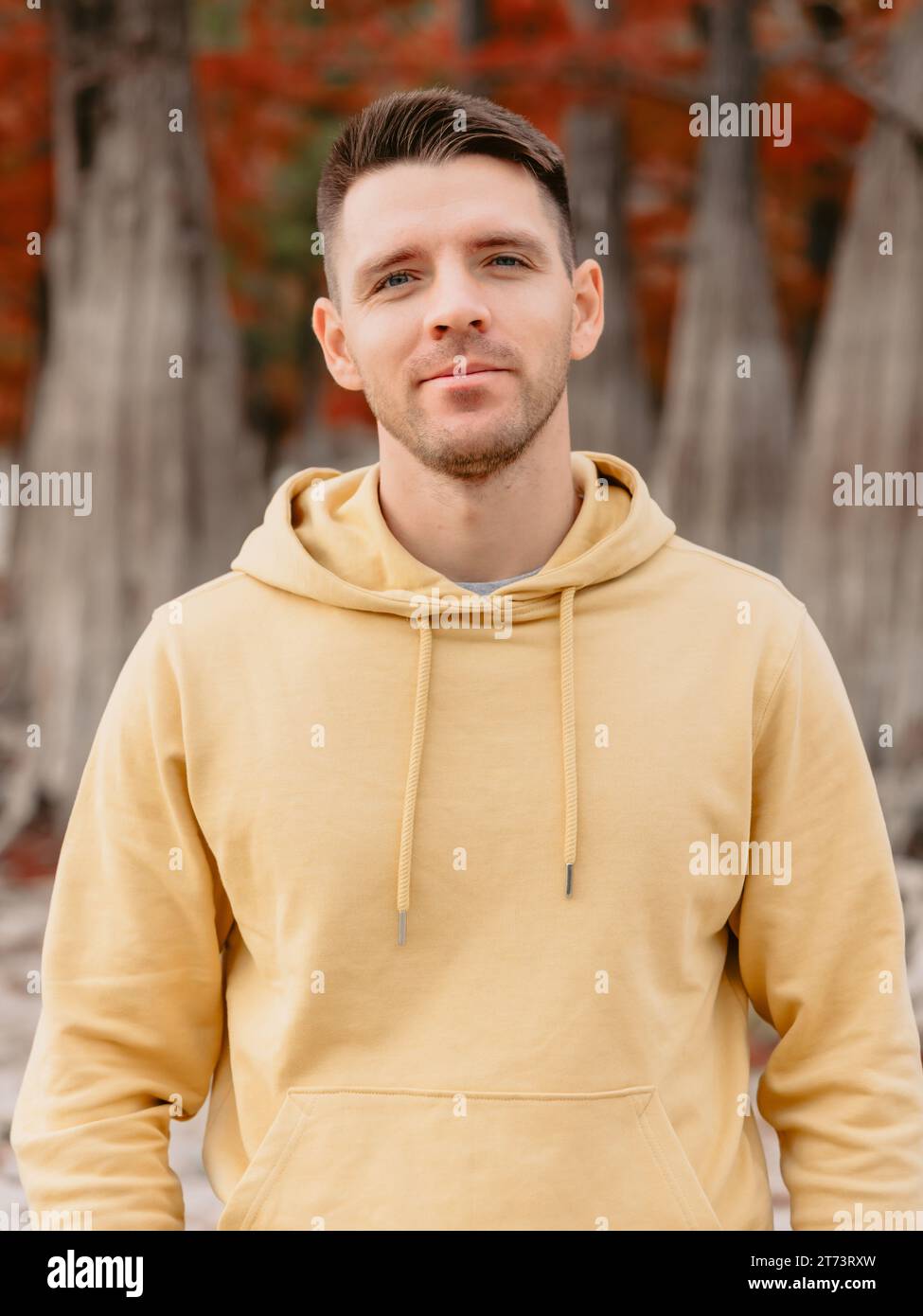 Schöner Mann, der im herbstlichen Wald in die Kamera schaut. Junger Mann in gelben Kapuzenpullis Stockfoto