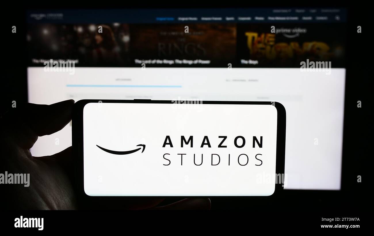Person mit Handy mit Logo der amerikanischen Film- und Fernsehproduktionsfirma Amazon Studios vor der Webseite. Schwerpunkt auf dem Display des Telefons. Stockfoto