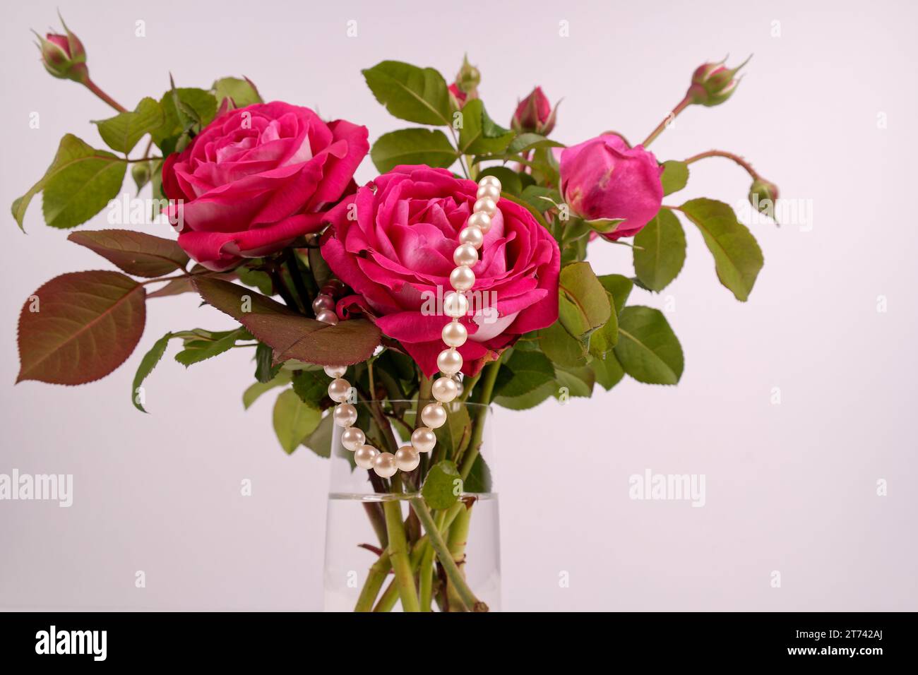 Ein Strauß aus verschiedenen roten Rosen mit grünen Blättern in einer Vase und eine Perlenkette, die eine Ehe symbolisiert Stockfoto