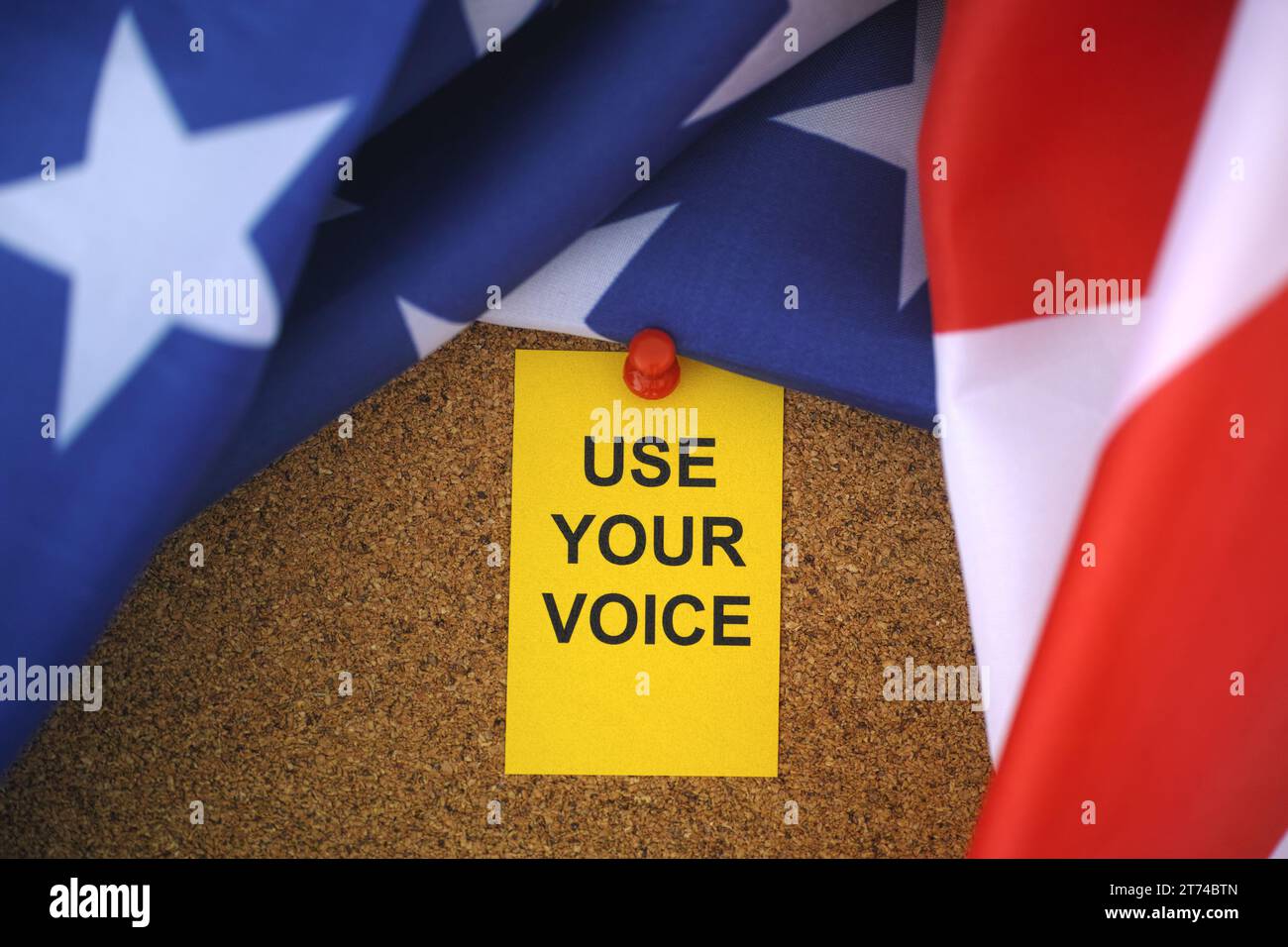 Die Flagge der USA und die gelbe Papiernote mit dem Slogan Use Your Voice drauf, die an ein Korkbrett angehängt ist. Nahaufnahme. Stockfoto