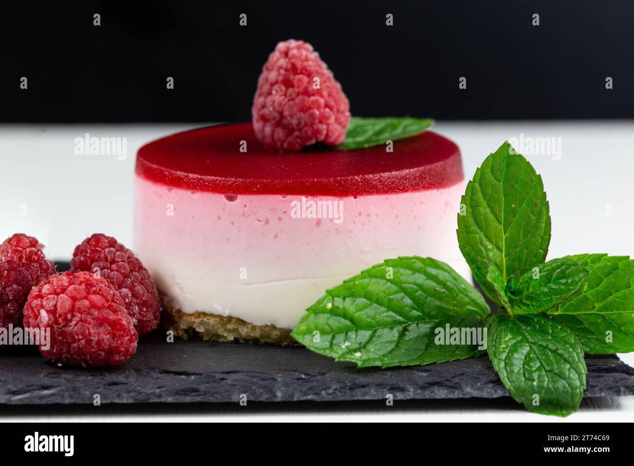 Ein köstlicher Himbeer-Käsekuchen mit frischen Himbeeren und Minzblättern auf einem schwarzen Schieferteller. Stockfoto