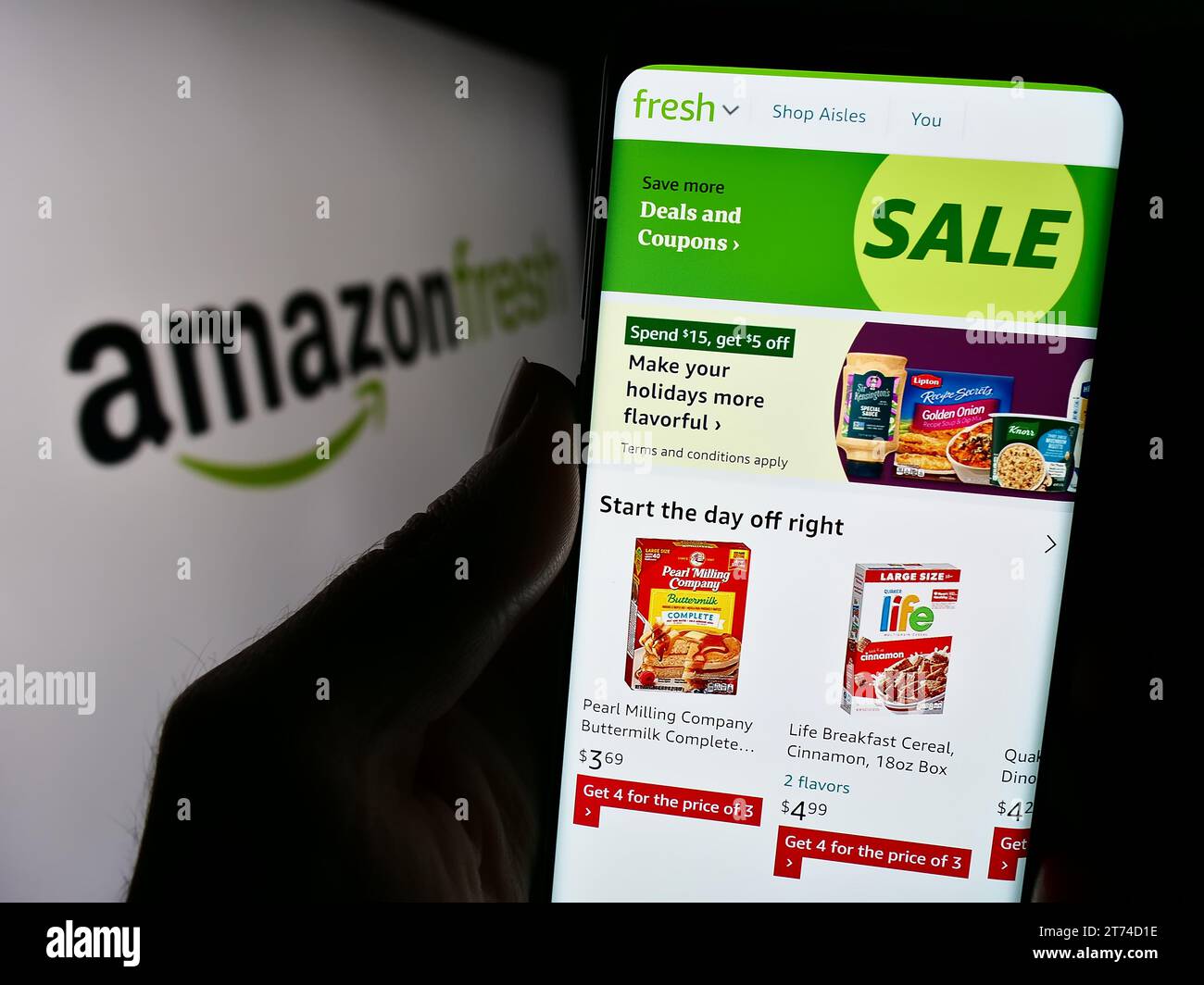 Person, die ein Mobiltelefon mit der Webseite des US-Lebensmitteleinzelhandelsunternehmens Amazon Fresh vor dem Firmenlogo hält. Konzentrieren Sie sich auf die Mitte des Telefondisplays. Stockfoto
