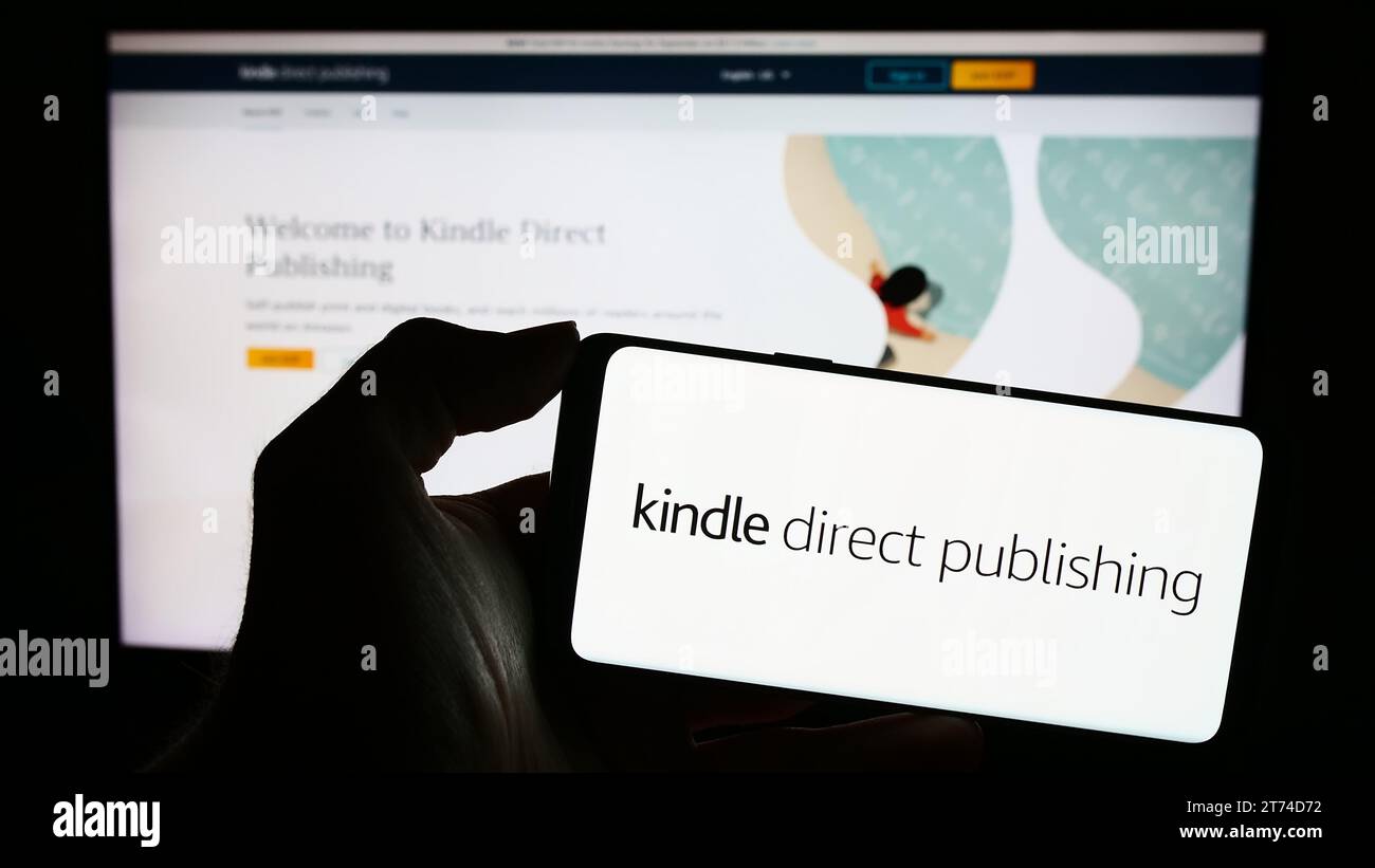 Person, die ein Mobiltelefon mit dem Logo der Amazon E-Book-Plattform Kindle Direct Publishing (KDP) vor der Webseite hält. Schwerpunkt auf dem Display des Telefons. Stockfoto