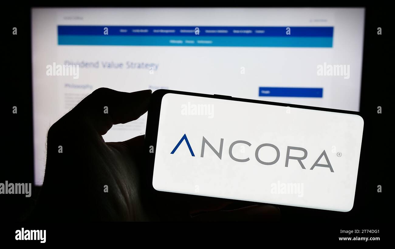 Person, die ein Mobiltelefon mit dem Logo der US-amerikanischen Investmentgesellschaft Ancora Holdings Group LLC vor der Webseite des Unternehmens hält. Schwerpunkt auf dem Display des Telefons. Stockfoto