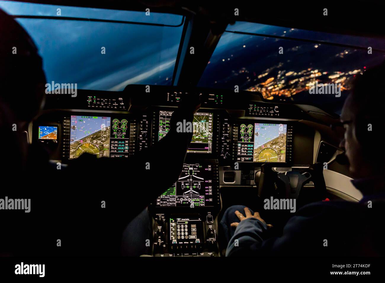 Blick aus dem Cockpit eines modernen Flugzeugs, das bei Nacht in einer beleuchteten Vilage landet. Beleuchtetes Cockpit-Armaturenbrett aus Glas bei der Landung am Flughafen Stockfoto
