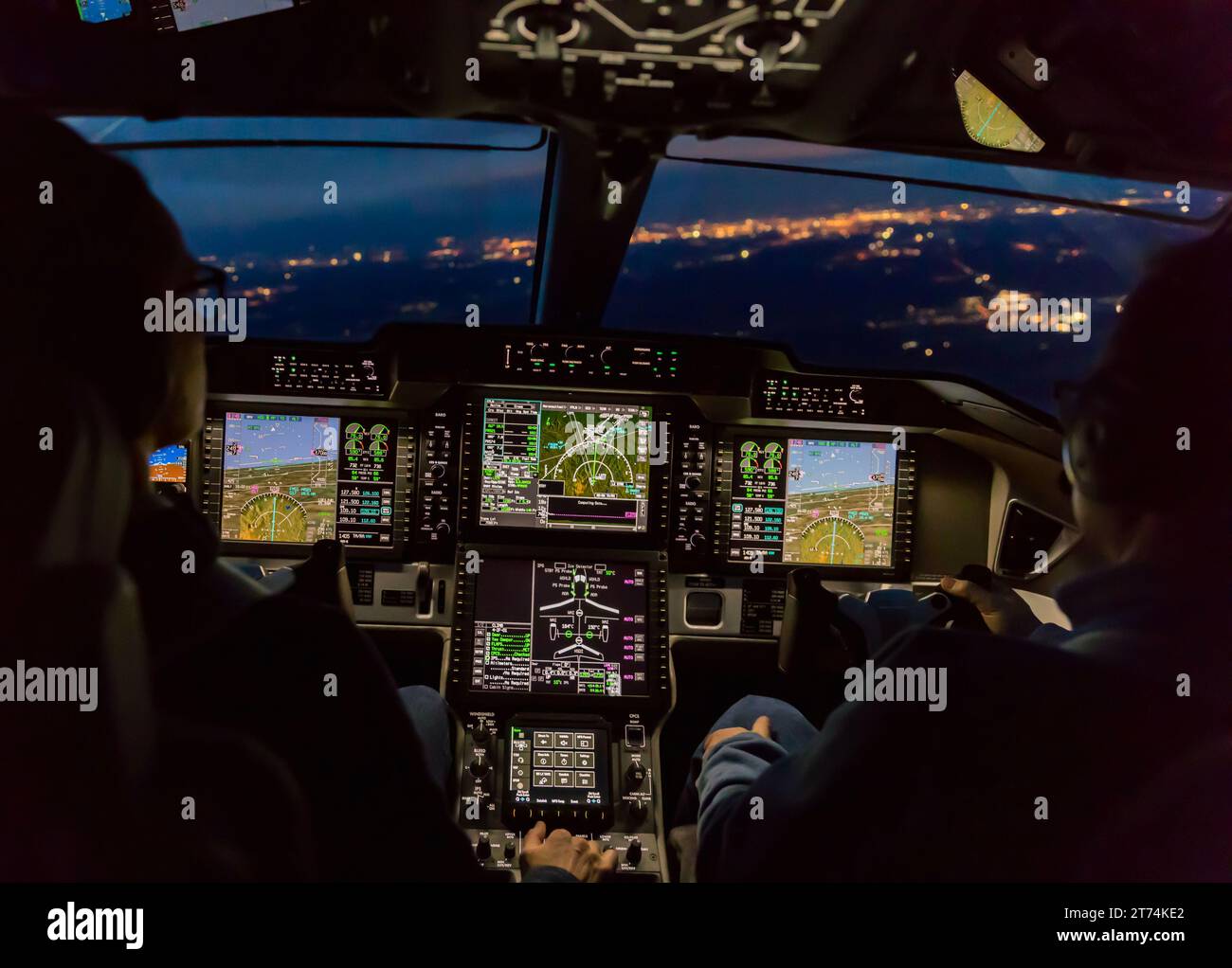 Blick aus dem Cockpit eines modernen Flugzeugs, das bei Nacht in einer beleuchteten Vilage landet. Beleuchtetes Cockpit-Armaturenbrett aus Glas bei der Landung am Flughafen Stockfoto