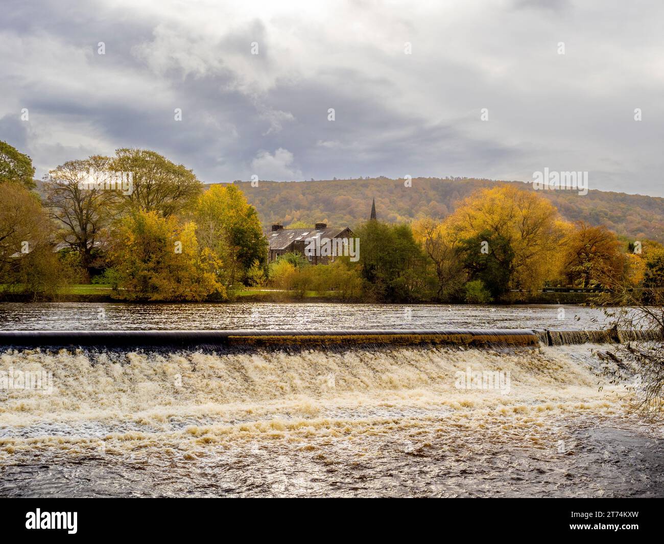 Das Wehr am River Wharfe in Otley, mit der herbstlichen Landschaft des Otley Chevin Forest Park in der Ferne. Stockfoto