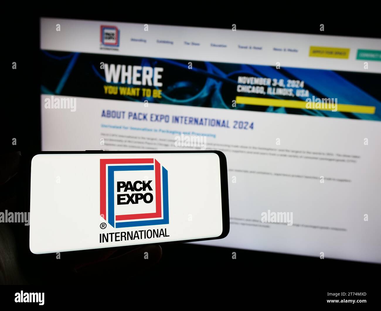 Person, die ein Mobiltelefon mit dem Logo der US-Messe EXPO International vor der Business-Website hält. Schwerpunkt auf dem Display des Telefons. Stockfoto