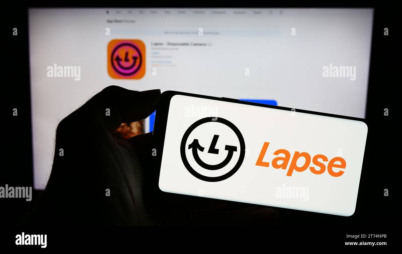 Person, die ein Mobiltelefon mit dem Logo der Einweg-Kamera-App Lapse vor der Webseite hält. Schwerpunkt auf dem Display des Telefons. Stockfoto