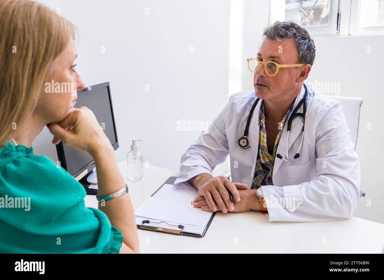Männlicher Arzt, der seinem Patienten ihre Diagnose in seiner Arztpraxis erzählt Stockfoto