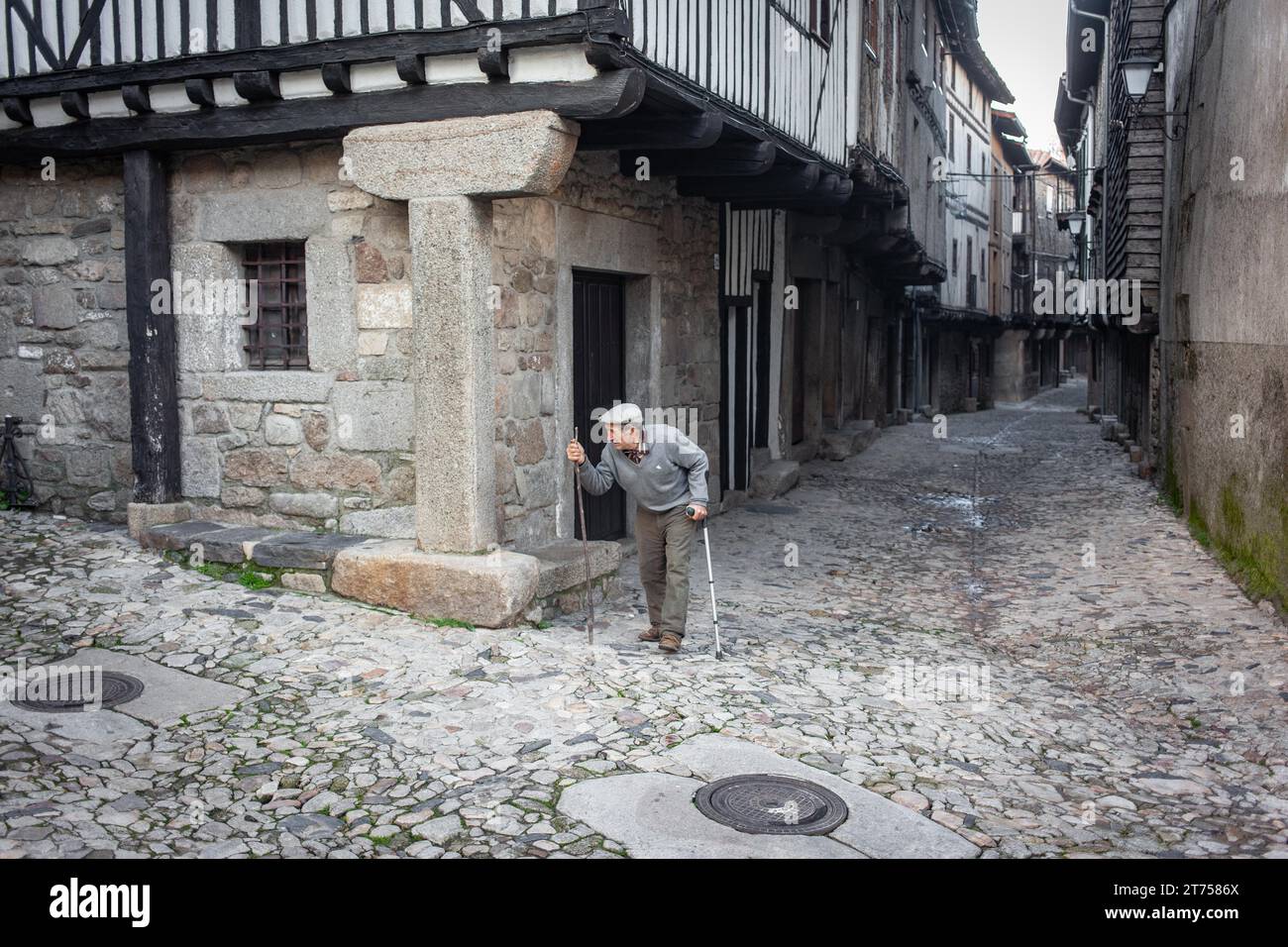 Alter Mann mit Krücken und Gehstock in einer Gasse in La Alberca, Salamanca, Spanien Stockfoto