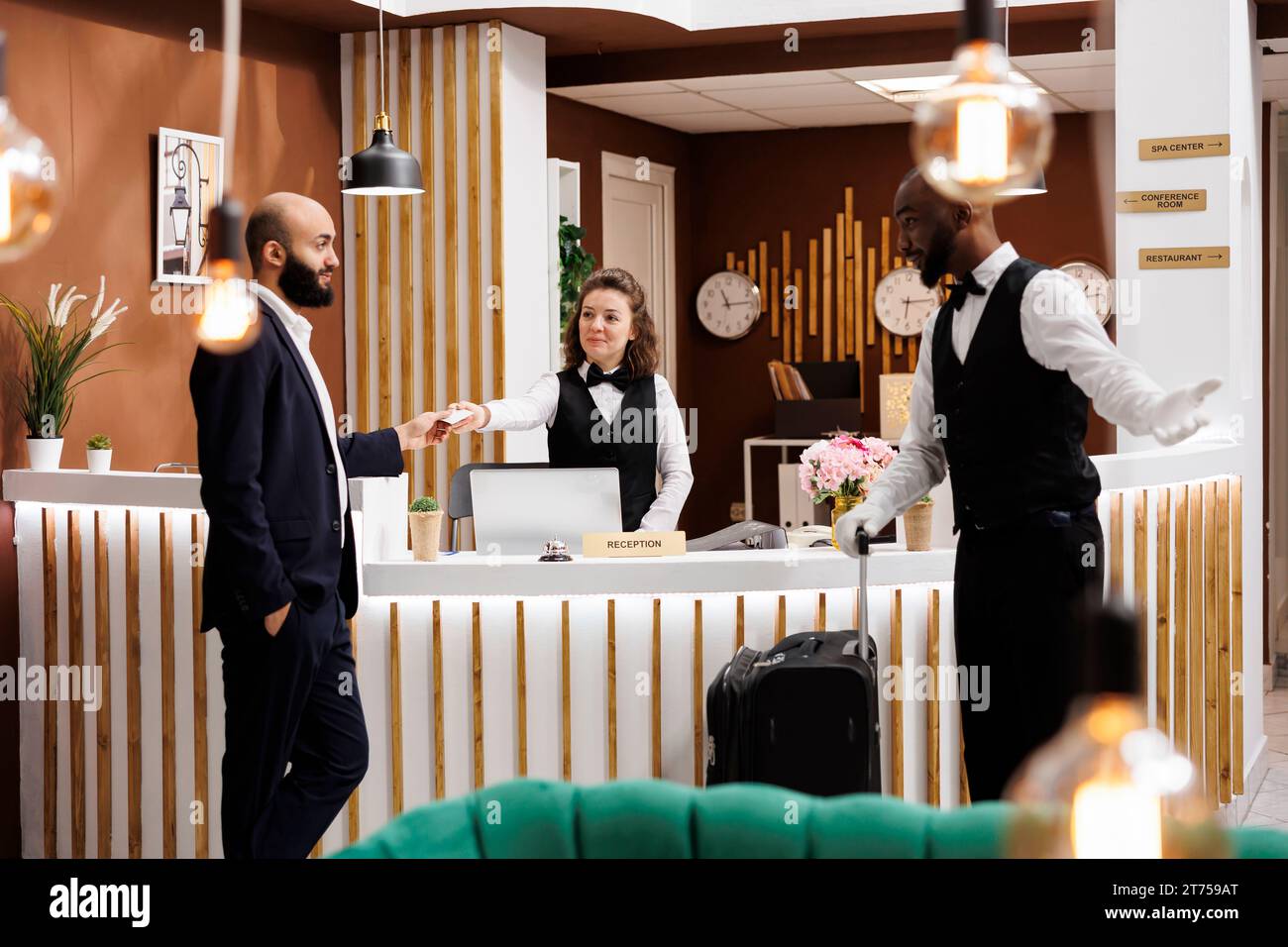 Geschäftsmann erhält in der Hotellobby eine Eintrittskarte, an der Rezeption stehen verschiedene Mitarbeiter zur Verfügung, die Gästen bei ihrer Ankunft luxuriöse Dienstleistungen anbieten. Angestellte, die im Resort willkommen geheißen werden, auf Geschäftsreise. Stockfoto