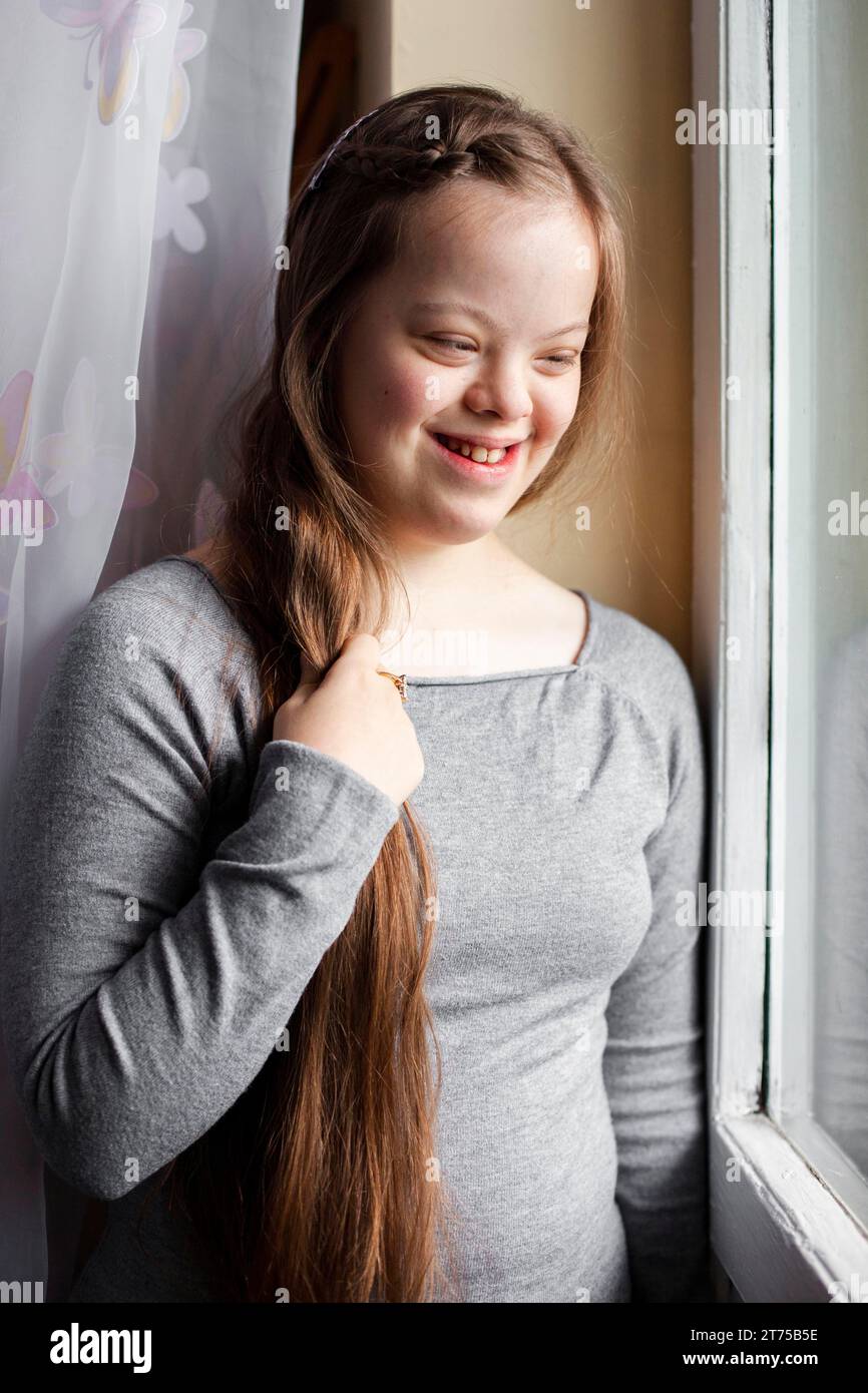 Smiley-Mädchen mit Down-Syndrom posiert am Fenster Stockfoto