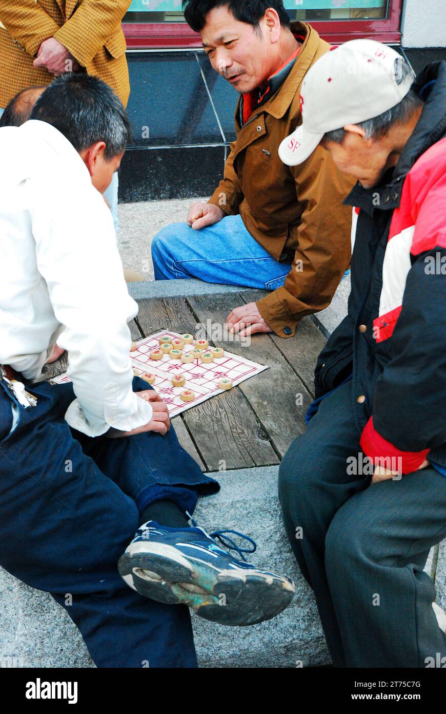Eine Gruppe von Freunden diskutiert Strategie, während sie in einem Stadtpark Xiangqi, der Form des chinesischen Schachs, spielen Stockfoto