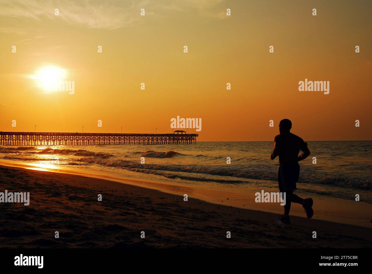 Ein erwachsener Mann trainiert und läuft entlang der Küste, während die Sonne am Himmel aufgeht, in der Nähe des Piers in Myrtle Beach Stockfoto