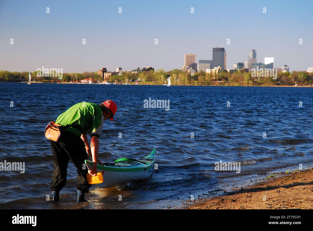 Ein erwachsener Kajakfahrer bereitet sich auf den Lake Calhoun vor, in Sichtweite der Skyline von Minneapolis Stockfoto