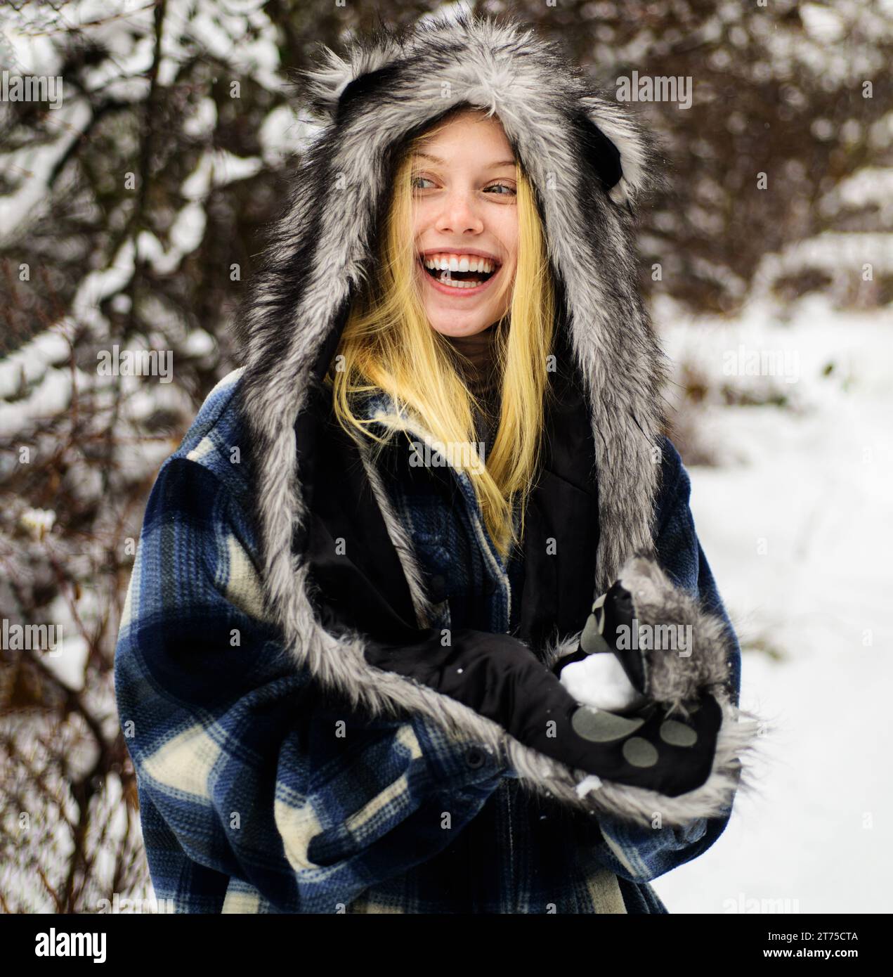 Winterzeit. Glückliche Frau im schneebedeckten Winterpark in warmer Kleidung mit Schneeball in den Händen. Lächelndes Wintermädchen, das mit Schnee spielt. Schönes weibliches Model in Stockfoto