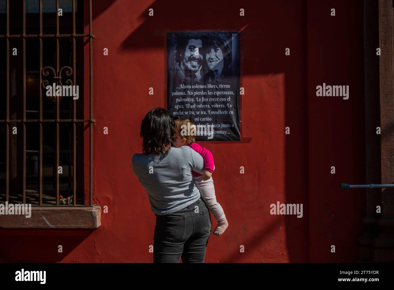 Eine Frau hält ihr Baby, während sie ein Bild mit den Gesichtern von Vctor Jara und seiner Frau Joan Jara ansieht. Während einer Spur von Joan Jara Turner. Tänzerin und Menschenrechtsaktivistin. Frau von Vctor Jara starb im Alter von 96 Jahren, nachdem sie 50 Jahre für Gerechtigkeit für ihren Geliebten kämpfte. 13. November 2023, Santiago de Chile. Santiago Chile Copyright: XClaudioxAbarcaxSandovalx Credit: Imago/Alamy Live News Stockfoto