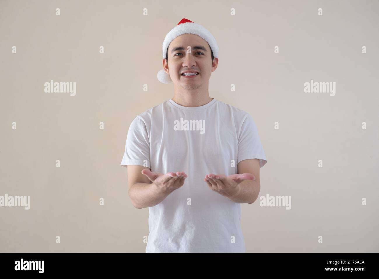 Der junge asiatische Weihnachtsmann öffnet seine Handflächen zur Kamera mit einem Lächeln auf isoliertem beigefarbenem Hintergrund. Weihnachtskonzept. Stockfoto