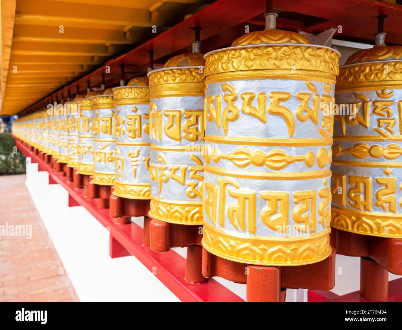 Eine Reihe kunstvoll verzierter goldener und silberner Gebetsmühle, die sich an der Wand eines buddhistischen Tempels aneinander Reihen Stockfoto