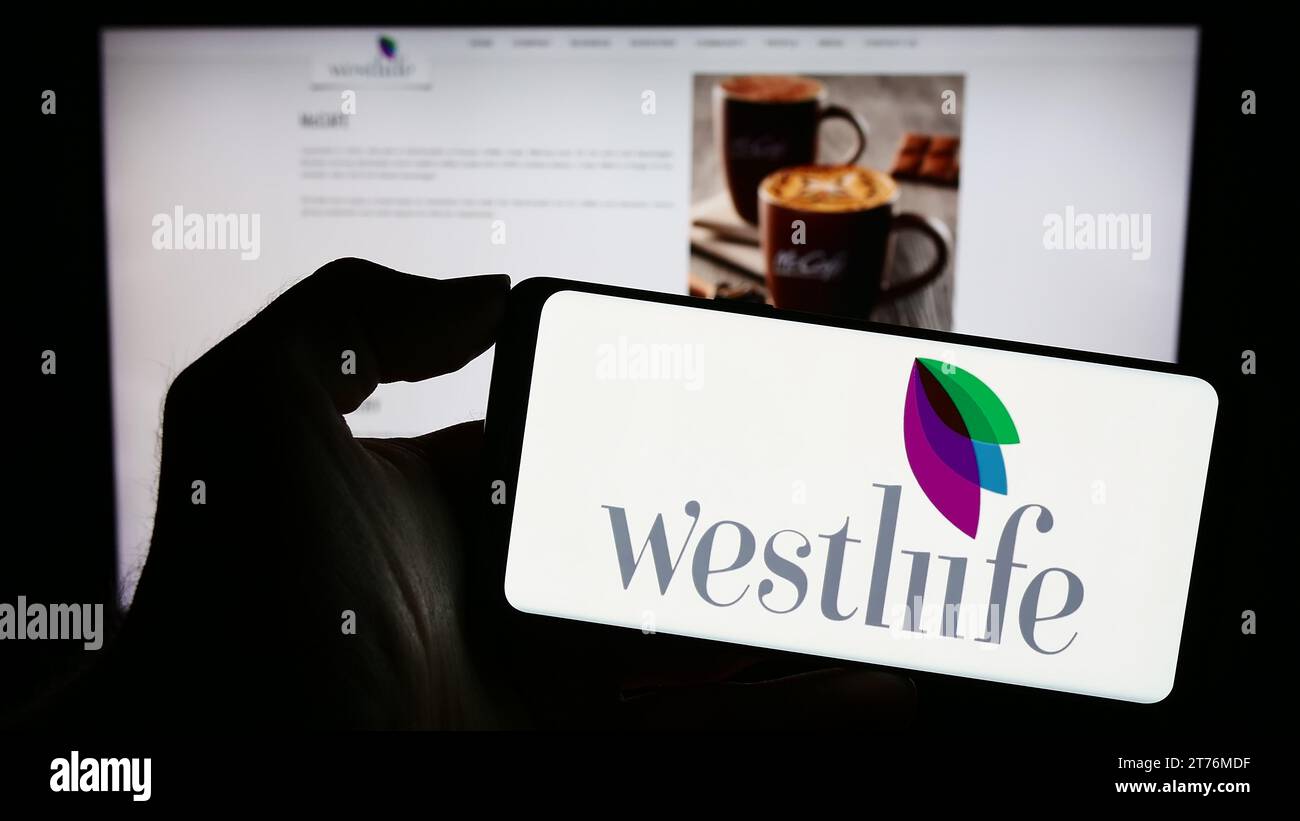 Person, die ein Mobiltelefon mit dem Logo des indischen Fast-Food-Unternehmens Westlife Foodworld Limited vor der Webseite hält. Schwerpunkt auf dem Display des Telefons. Stockfoto