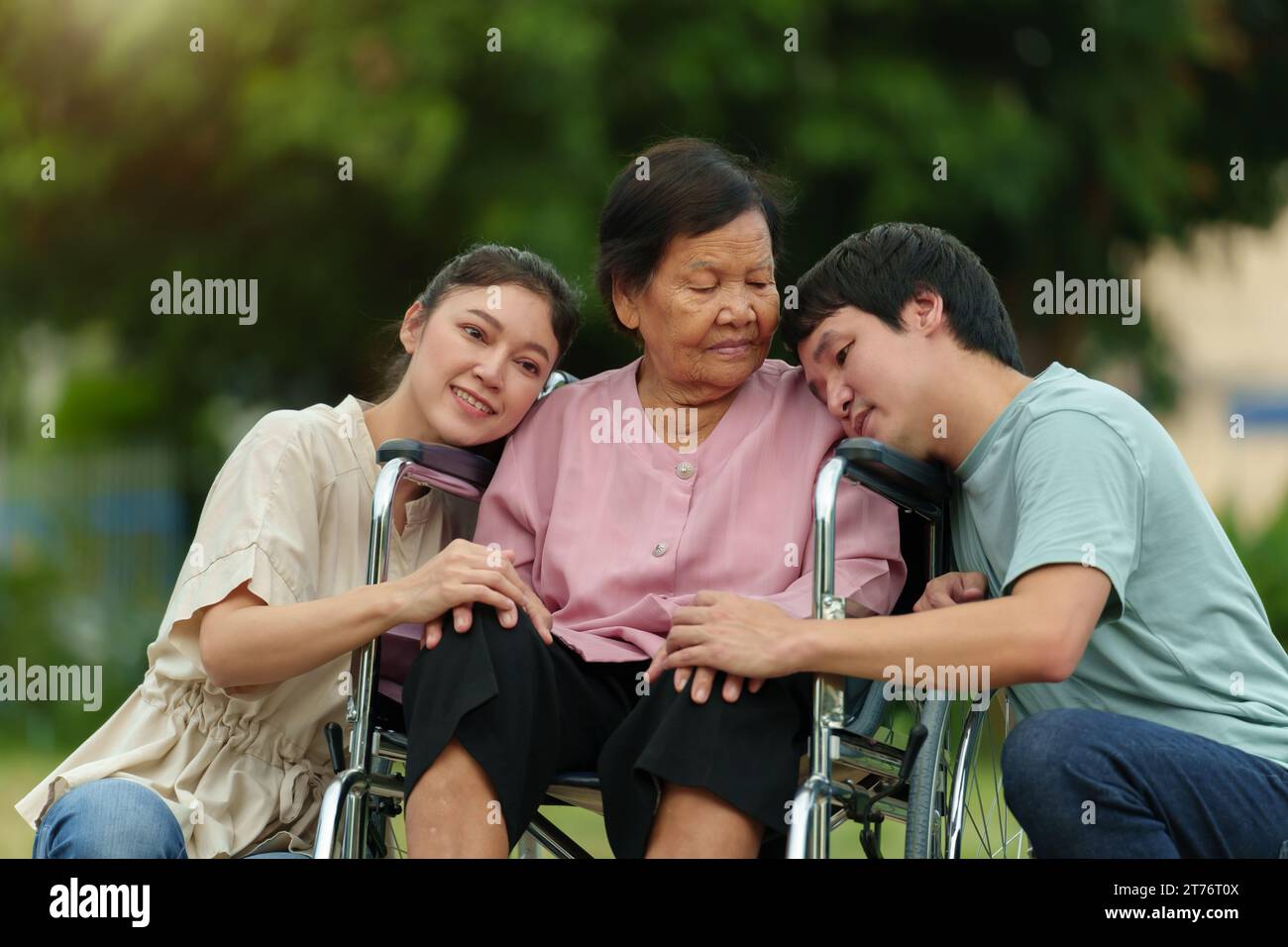 Glücklicher Enkel und Enkelin mit Seniorin im Rollstuhl im Park Stockfoto