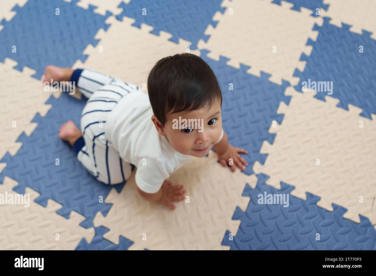 Blick von oben auf das glückliche Baby, das auf der Spielmatte oder dem Puzzle-Boden krabbelt Stockfoto