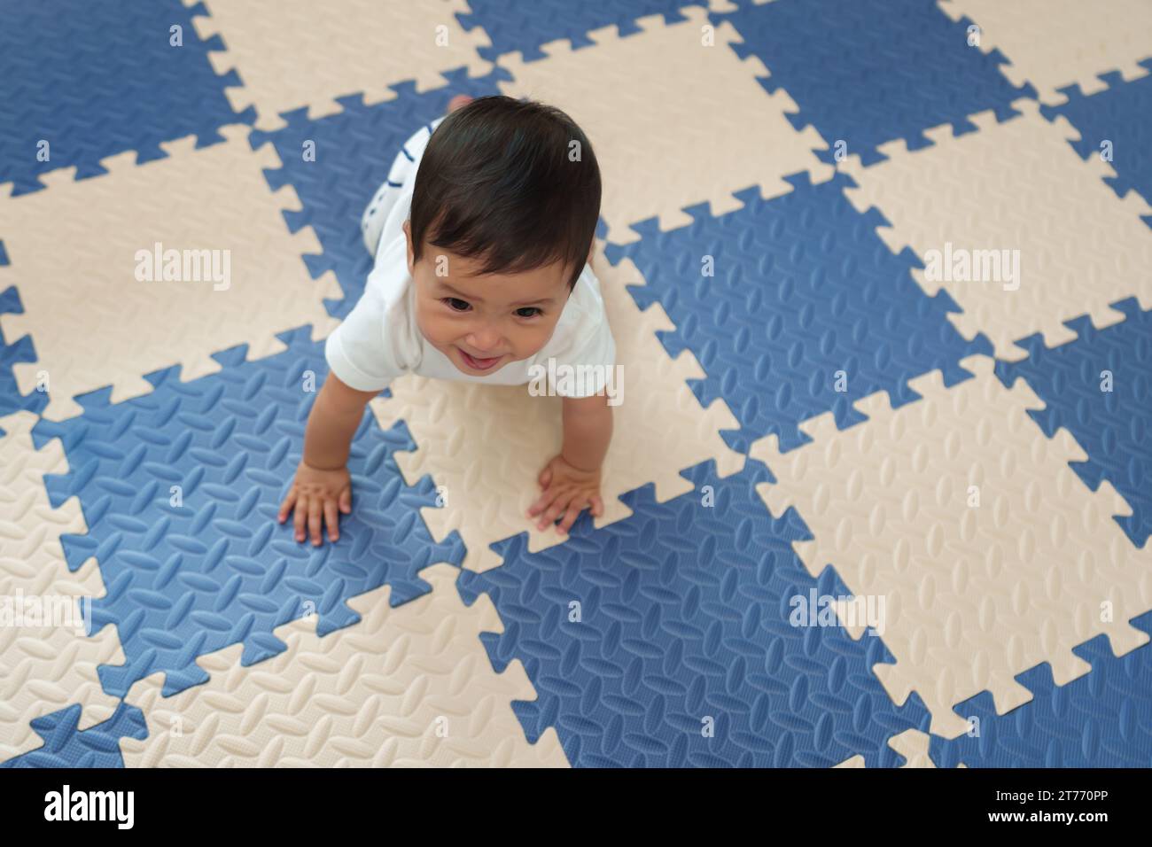 Blick von oben auf das glückliche Baby, das auf der Spielmatte oder dem Puzzle-Boden krabbelt Stockfoto