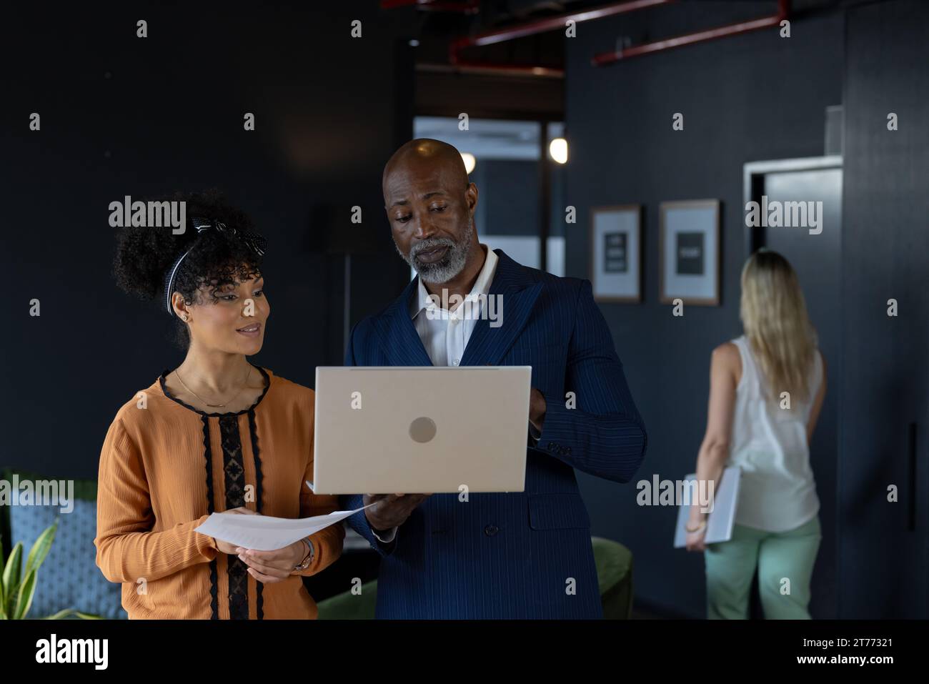 Glückliche, vielfältige Kollegen, die einen Laptop benutzen und Dokumente im Büro diskutieren Stockfoto