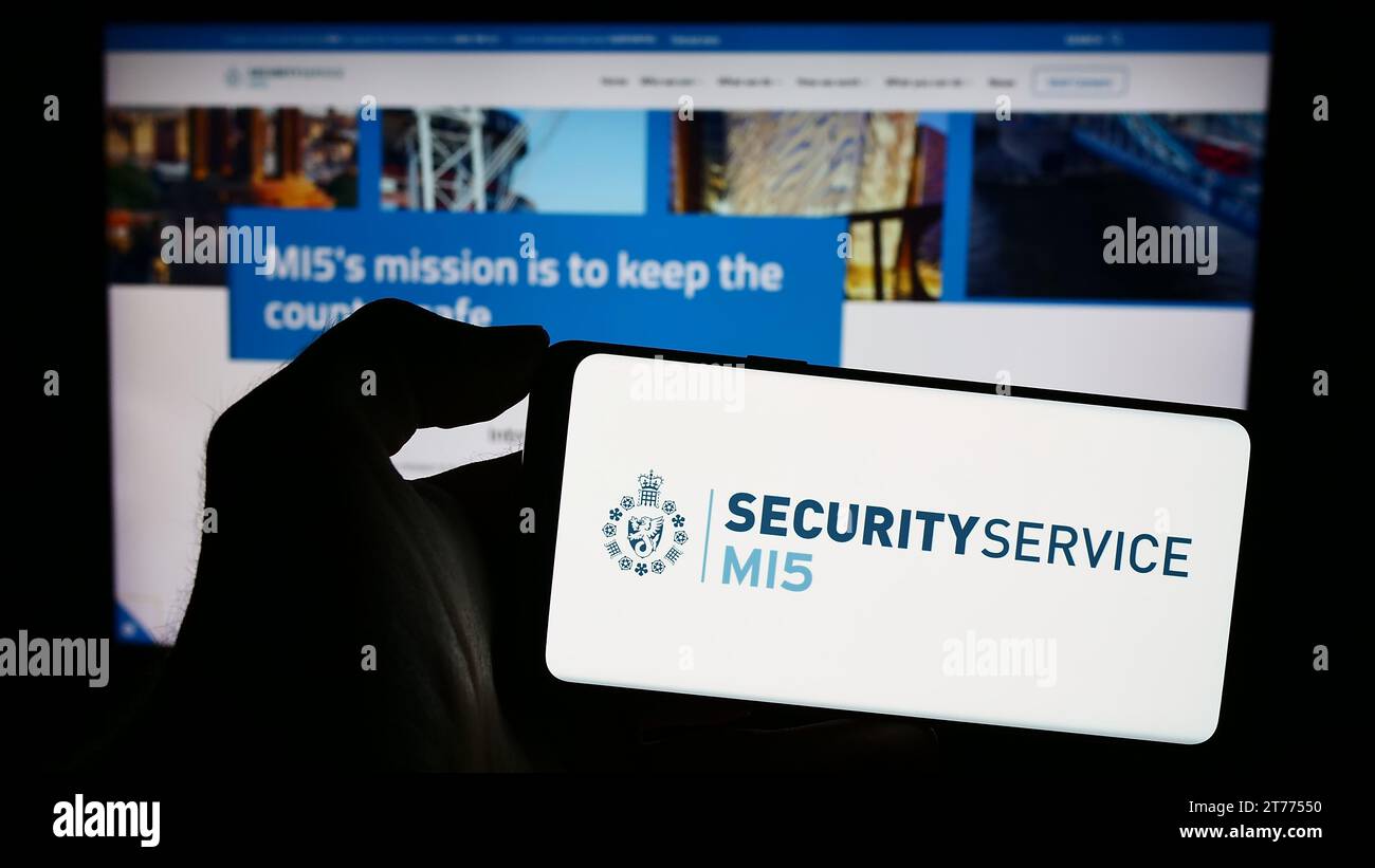 Person, die ein Mobiltelefon mit dem Logo der britischen Geheimdienstabwehr Security Service (MI5) vor der Webseite hält. Schwerpunkt auf dem Display des Telefons. Stockfoto