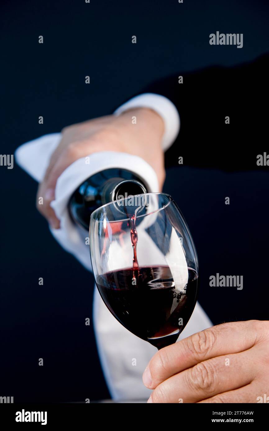 Nahaufnahme von einem Kellner Hände halten Sie eine Flasche und einem Glas Rotwein herein Stockfoto