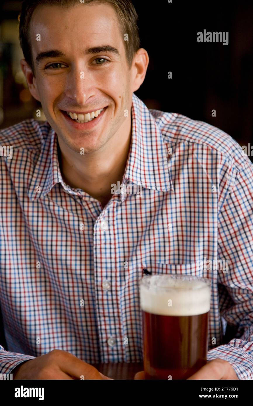 Ein lächelnder Mann sitzt und hält ein Bier Stockfoto