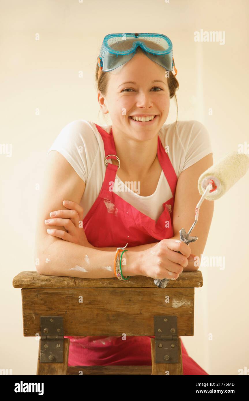 Porträt einer lächelnden Frau stehen auf einer Leiter mit einem Farbroller Stockfoto