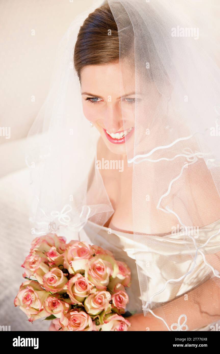 Lächelnde Braut, die einen Schleier trägt und einen Rosenstrauß hält Stockfoto