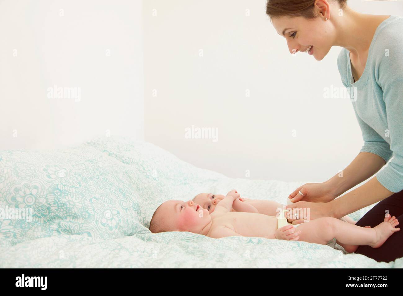 Lächelnde Mutter kniend auf Bett Zwillingen spielen Stockfoto