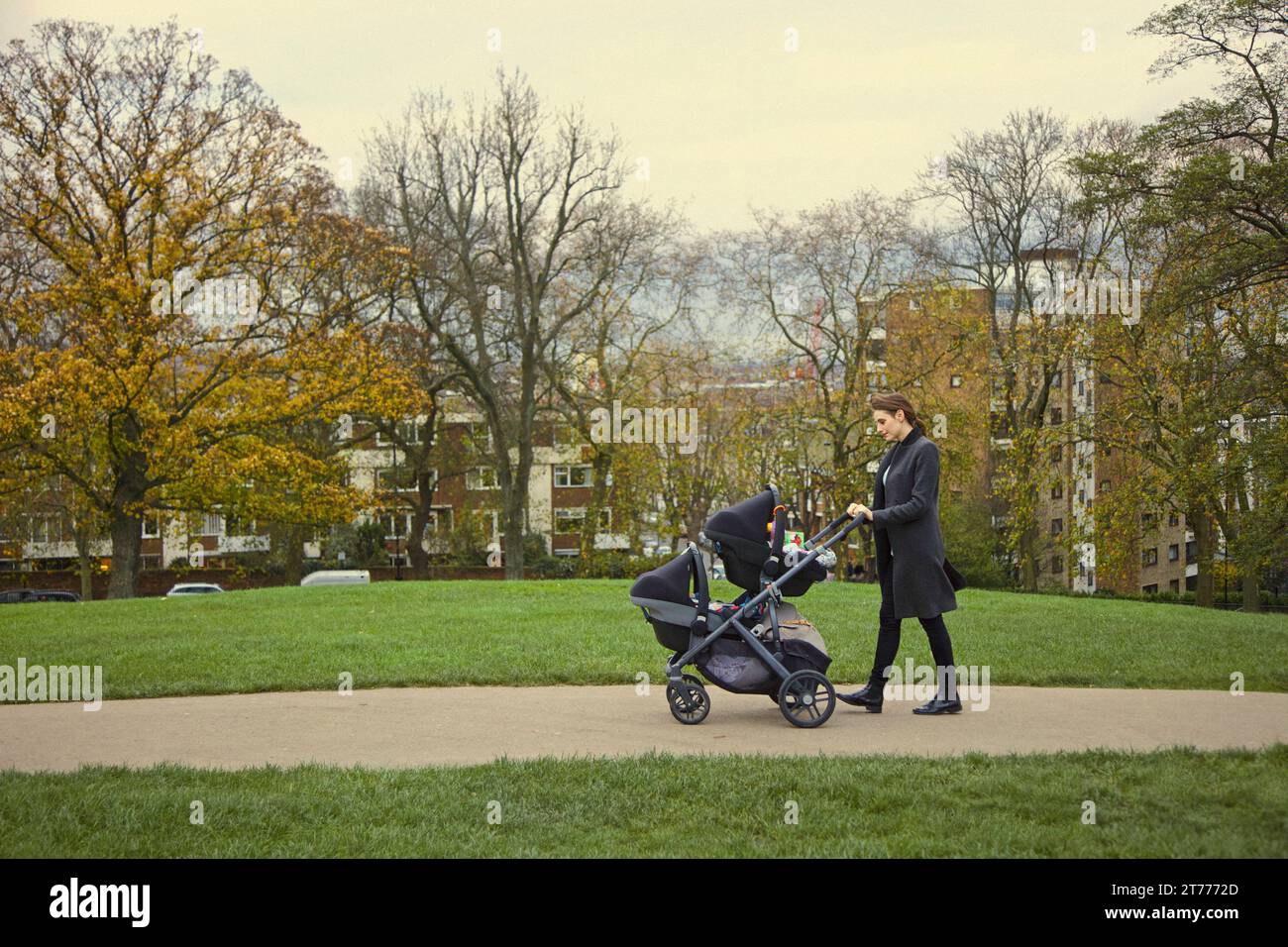 Mutter drückt Doppel-Kinderwagen im Stadtpark Stockfoto