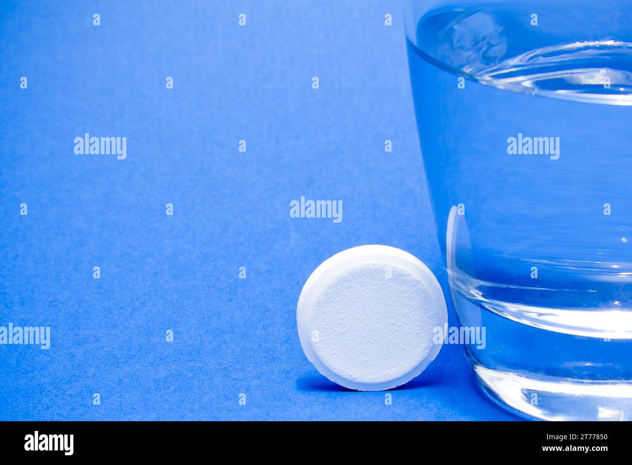 Wasserglas in der Nähe einer Tablette auf blauem Hintergrund Stockfoto