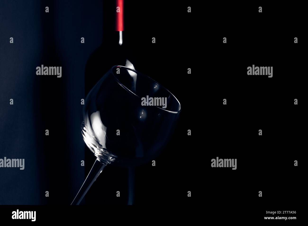 Weinglas vor der Flasche in der Nähe des Schattens in dunkelblauem Licht mit Platz für Text Stockfoto