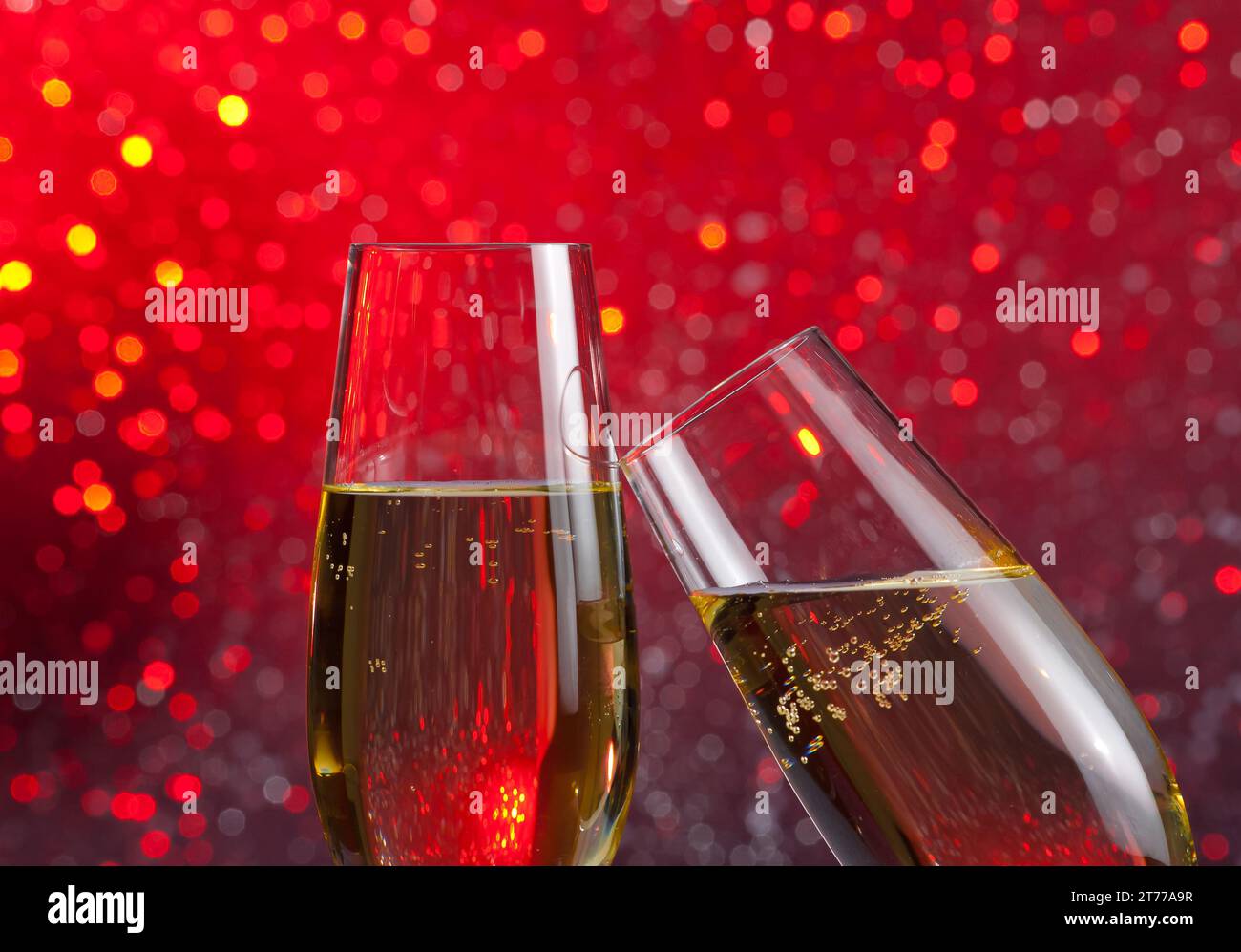 Zwei Sektflöten mit goldenen Luftblasen geben Anfeuerungen auf rotem Bokeh-Hintergrund mit Platz für Text Stockfoto