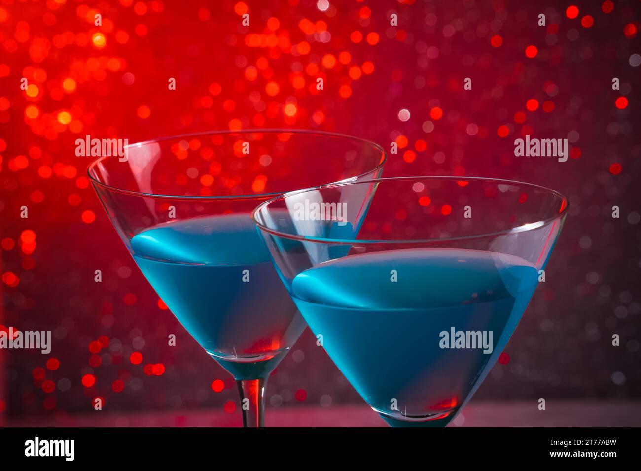 Detail eines Brillenglases blauer Cocktail auf rotem, hellem Bokeh-Hintergrund Stockfoto