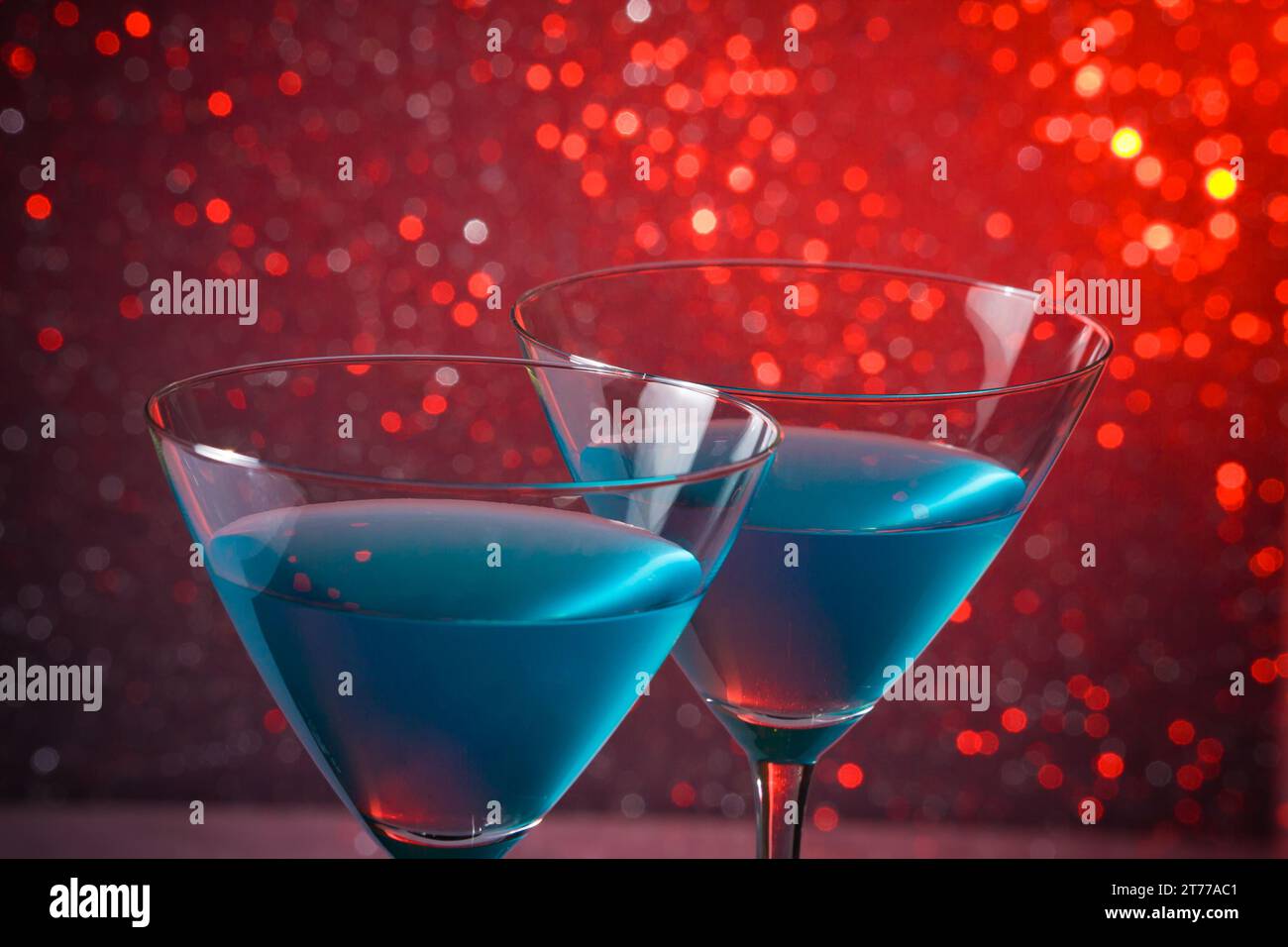 Detail eines Brillenglases blauer Cocktail auf rotem, hellem Bokeh-Hintergrund Stockfoto