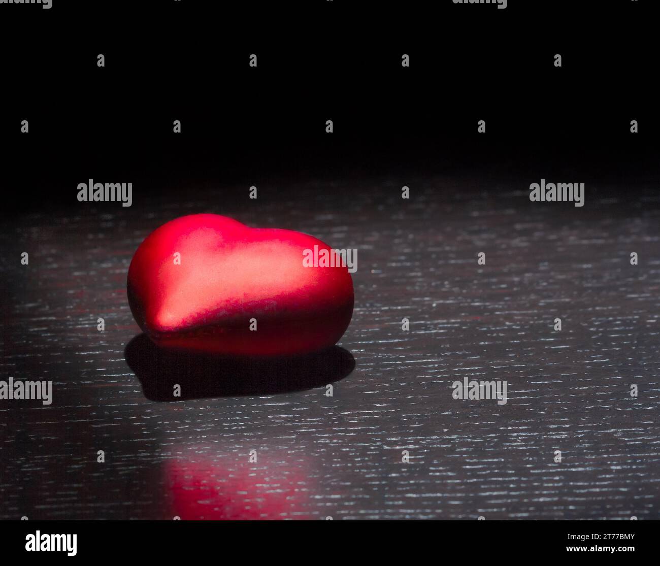 Ein dekoratives rotes Herz auf schwarzem dunklem Licht und auf Holztisch mit Platz für Text, valentinstag-Konzept Stockfoto